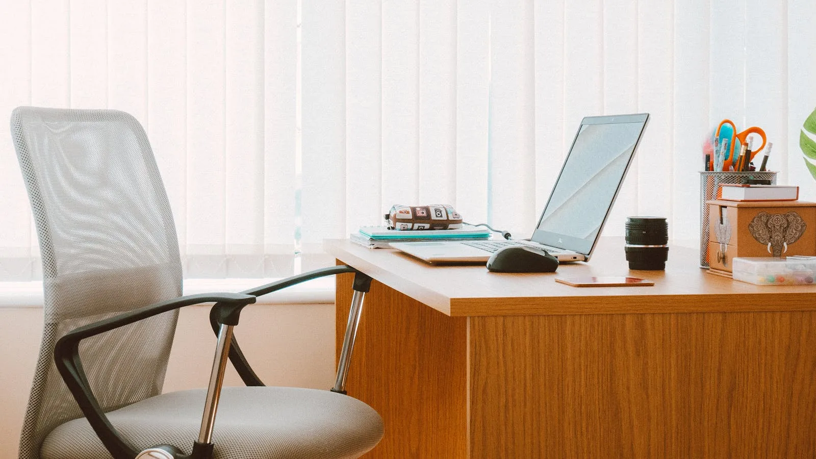 Modern mesh-back office chair next to a wooden desk with a laptop