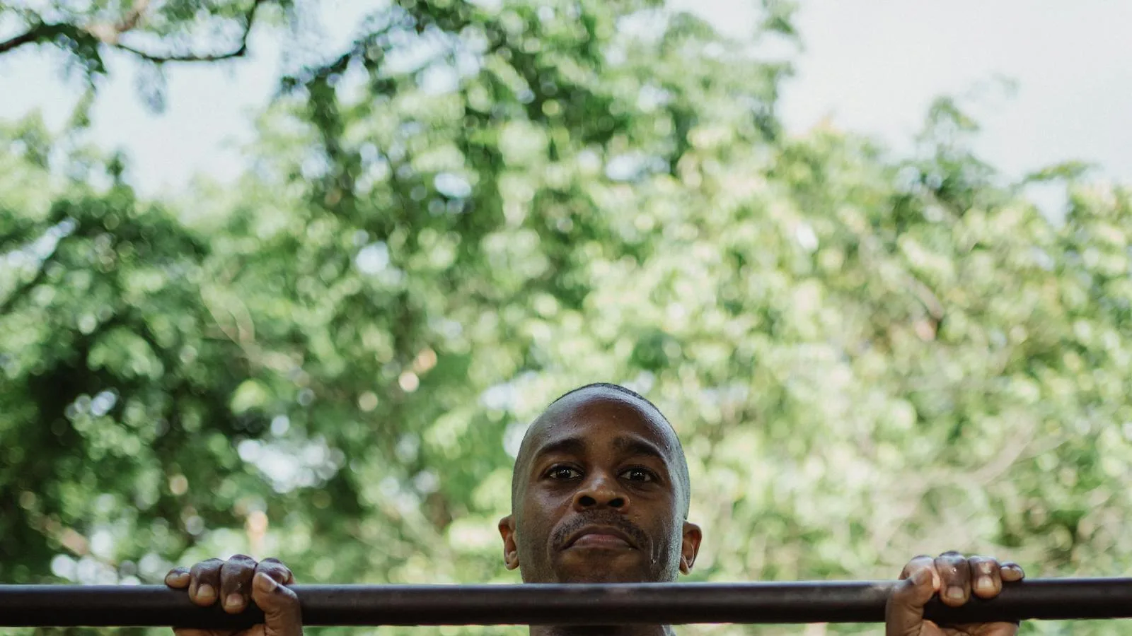 Person gripping a pull-up bar outdoors in a leafy park