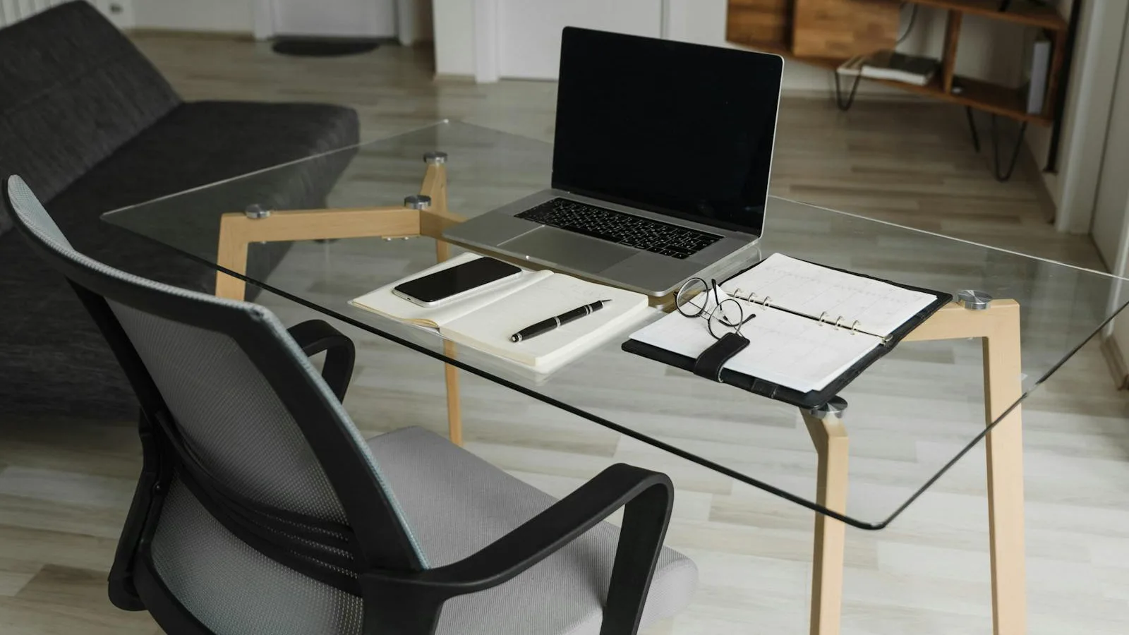 Glass desk with a laptop, planner, and pen in a softly lit room