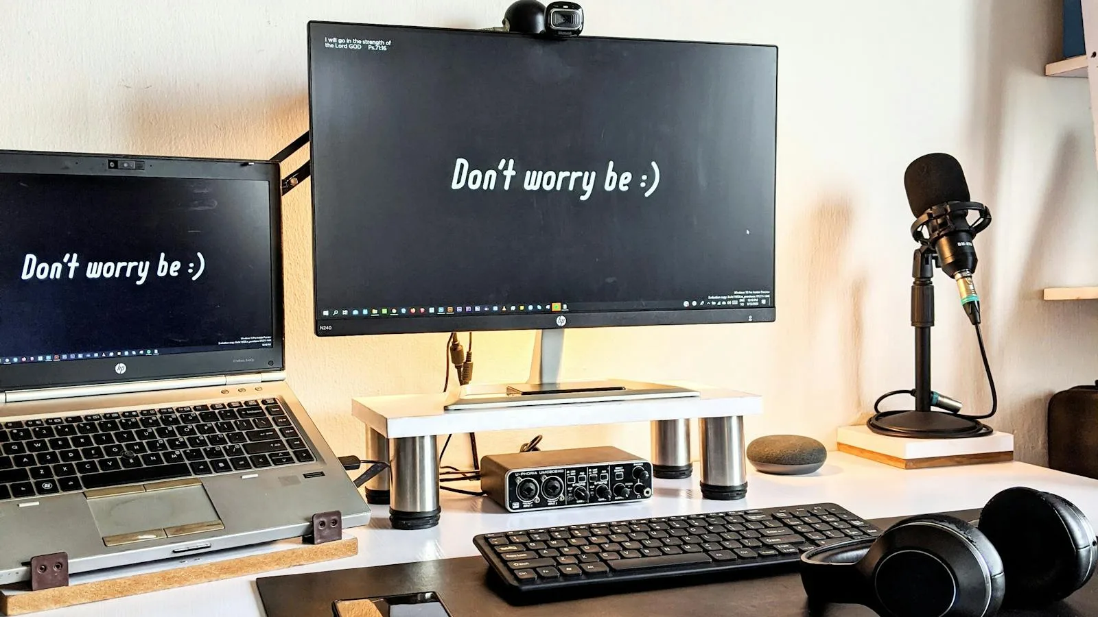 Modest dual-monitor desk setup with laptop, microphone, and headphones
