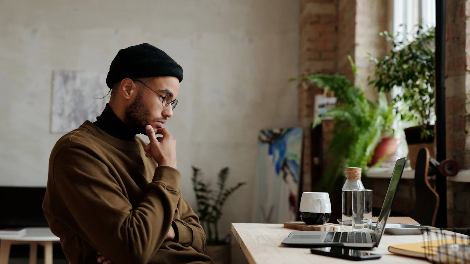 Focused person thinking with hand on chin at a laptop in a quiet room